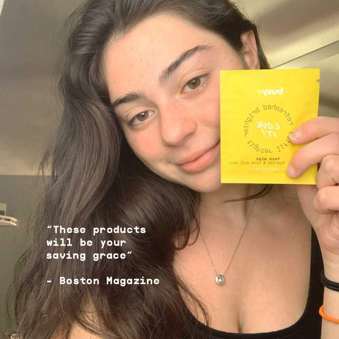 Smiling woman holding up yellow Busy Beauty packaging with a Boston Magazine quote